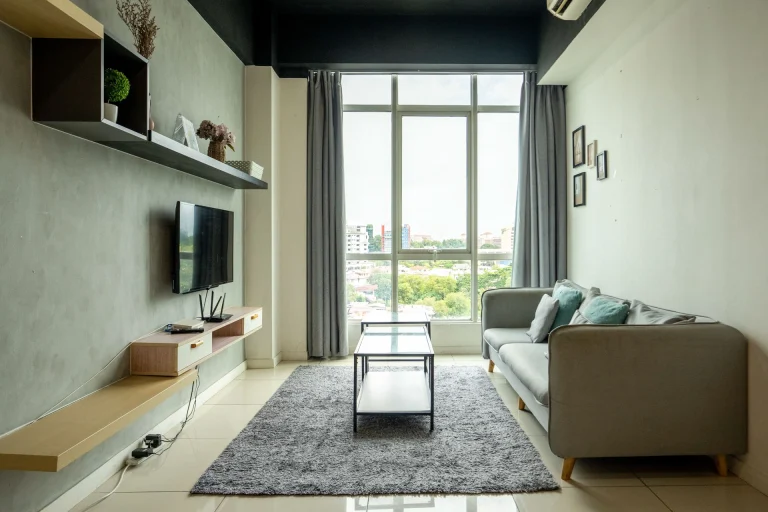 Modern living room with gray sectional sofa, floating shelves, and large windows overlooking urban cityscape views