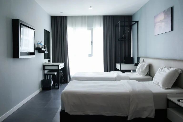 Clean modern hotel bedroom featuring separate beds, entertainment center, desk space, and large windows
